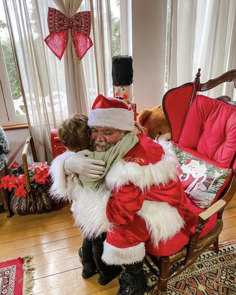 papai noel abraçando uma criança dentro d casa do papai noel em campos do jordão