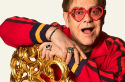 elton john sentado em uma cadeira dourada em frente a um fundo branco